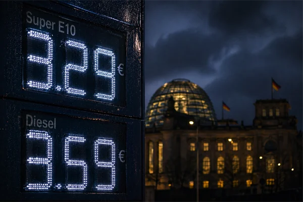 Preisanzeige einer Tankstelle in der Nacht: Super E10 für 3,29 Euro und Diesel für 3,58 Euro pro Liter, im Hintergrund die beleuchtete Kuppel des Berliner Reichstagsgebäudes mit deutscher Flagge unter bewölktem Nachthimmel.